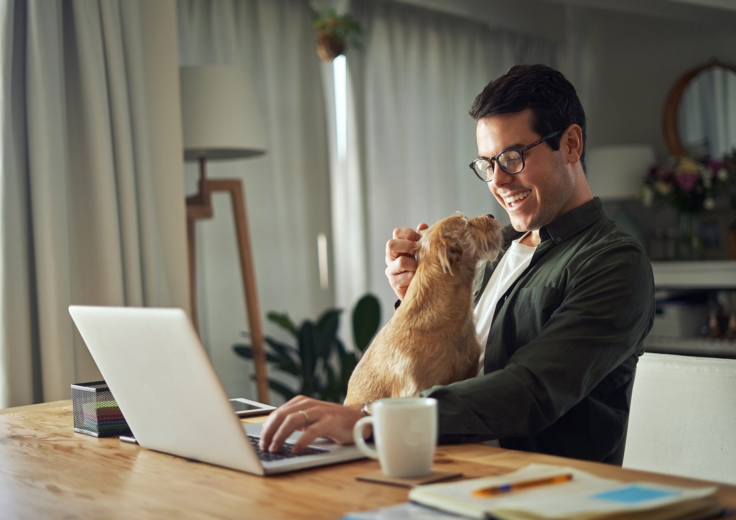Cheerful man playing with dog while using laptop_